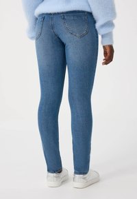 Niebieskie dżinsy skinny o gładkiej fakturze, z standardowymi tylniymi kieszeniami i dopasowanym krojem, w połączeniu z białymi sneakersami.