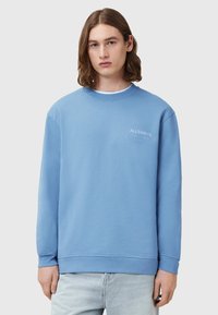 Světle modrá mikina vyrobená z bavlny, s kulatým výstřihem, dlouhými rukávy a malým vyšitým logem na hrudi. Jednoduchý design.