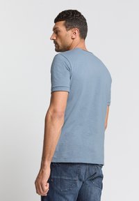 Lichtblauwe t-shirt met korte mouwen en een ronde halslijn, met een gladde textuur en een relaxte pasvorm, gecombineerd met donkerdenim jeans. Achteraanzicht.