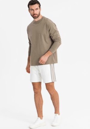 Langærmet olivengrøn skjorte med rund hals, parret med hvide shorts med en sort sidestribe. Båret med hvide sneakers.