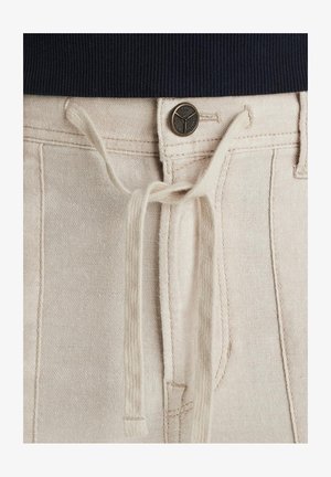 Pantaloni in cotone beige con coulisse, dotati di chiusura con bottone metallico, tasche frontali e vita in contrasto scuro. Tessuto liscio e testurizzato.