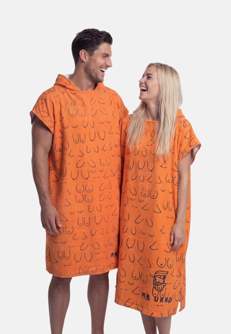 Hombre y mujer sonriéndose mutuamente, vestidos con togas naranjas con capucha y dibujos en líneas negras abstractas sobre un fondo blanco liso.