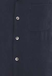 Navy-blaues Button-up-Hemd mit einer einzelnen Brusttasche, silbernen Knopfverschlüssen und einer glatten, matten Textur.