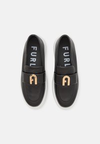 Zapatos de cuero negro tipo slip-on con un acento de hardware en color dorado y suela blanca, que cuentan con una parte superior acolchada para mayor comodidad y una plantilla con logo.