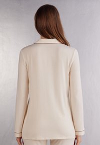Crème lange mouw top met een kraag, voorzien van contrasterende piping langs de kraag en manchetten. Zachte stof met een gladde textuur.