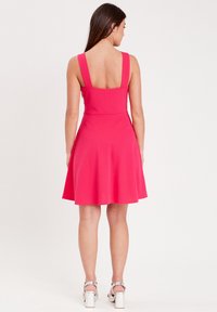 Un vestido sin mangas de color rosa brillante con un corsé ajustado y una falda acampanada, con tirantes anchos y una textura suave. Mostrado desde la parte de atrás.
