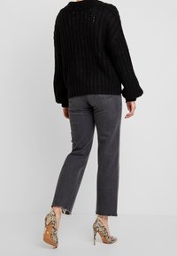 Svart stickad tröja med lös passform, i kombination med mörkgrå raka jeans. Skorna har ett ormtrycksmönster på klackarna.