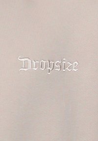 Cotton t-shirt in light beige with embroidered "Dropsize" text in white, featuring elegant font style and smooth fabric texture.