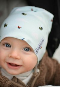 Pehmeä, vaaleansininen pipo, jossa on pieniä kuvioita mehiläisistä ja leppäkertuista. Valmistettu joustavasta kankaasta, sivussa on logo.