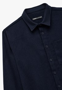 Marineblå flannel skjorte med spids krave, knaplukning foran og en enkelt brystlomme. Blød tekstur med subtile stofdetaljer.