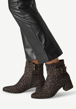 Knöchelhohe Stiefel mit Leopardenmuster, seitlichen Reißverschlüssen und großen runden Schnallen, getragen zu schwarzen, kurzen Lederhosen.