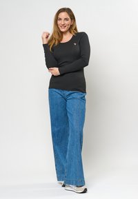 Svart ribbad långärmad topp med rund halsringning, kombinerad med vida blå denimjeans som har en avslappnad passform och en subtil logotypdetalj.
