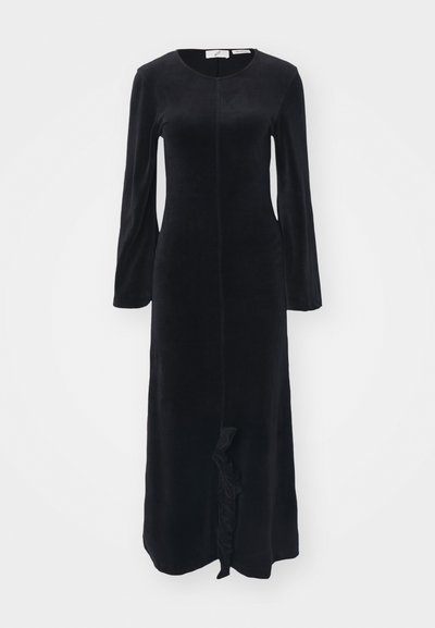 Robe longue noire à manches longues en tissu doux, avec un col rond, une coupe ajustée et un détail à volants au niveau de l'ourlet. Texture lisse sur toute la surface.