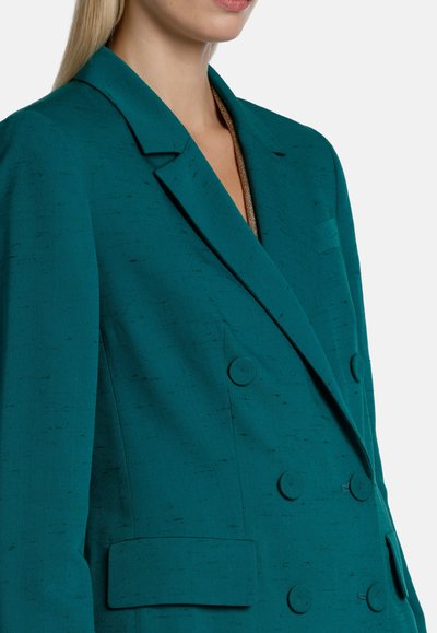Teal double-breasted blazer featuring a structured lapel, textured fabric, and two front pockets with circular buttons.