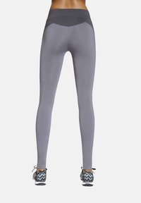 Szare legginsy z wysokim stanem z teksturowanym pasem, o gładkim wykończeniu i ciemnych kontrastujących akcentach z tyłu. Połączone z butami w wzory.