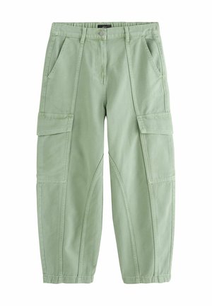 Persoană purtând pantaloni cargo largi verde deschis, top fără mâneci în dungi, sandale cu platformă maro, ceas și inele, stând pe un fundal neutru.