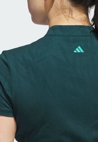 Mörkgrön atletisk tröja med texturerad design, med ett subtilt mönster och en turkos Adidas-logotyp på baksidan av kragen.