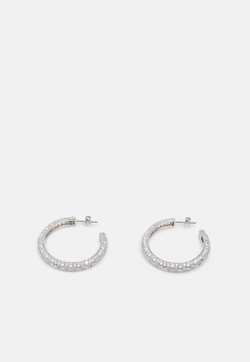 Boucles d'oreilles créoles ouvertes en argent incrustées de petites pierres précieuses claires, sécurisées par des fermoirs à tige, présentées sur un fond clair uni.