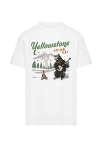 White t-shirt featuring a graphic of a bear playing banjo in front of mountains and trees, with "Yellowstone National Park" text in green and orange.