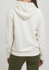 Sudadera color crema con un bolsillo tipo canguro, puños acanalados y capucha con cordón. Material suave con textura lisa, diseñada en un corte relajado.