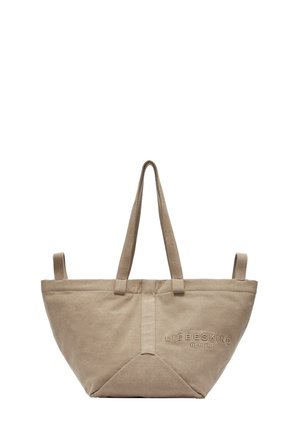 Sac tote en toile beige avec deux poignées, forme triangulaire, surface texturée et logo de la marque en relief sur le côté.