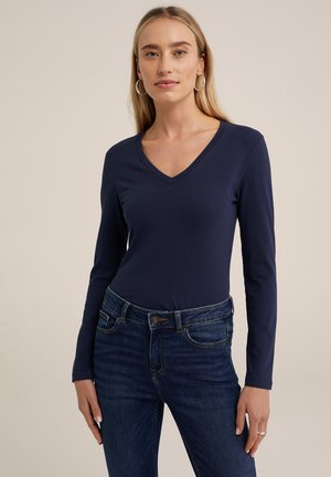 Navy langärmliges V-Ausschnitt-Shirt aus weichem Material, kombiniert mit blauen Jeans mit Knopfverschluss und gesteppten Akzenten.