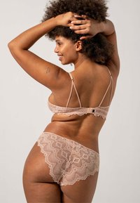 Pitsitää lace-lingeriesetti pehmeässä vaaleanpunaisessa, joka sisältää säädettävillä olkaimilla varustetun braletin ja yhdisteeseen sopivat alushousut, joissa on aaltoilevat pitsireunat.