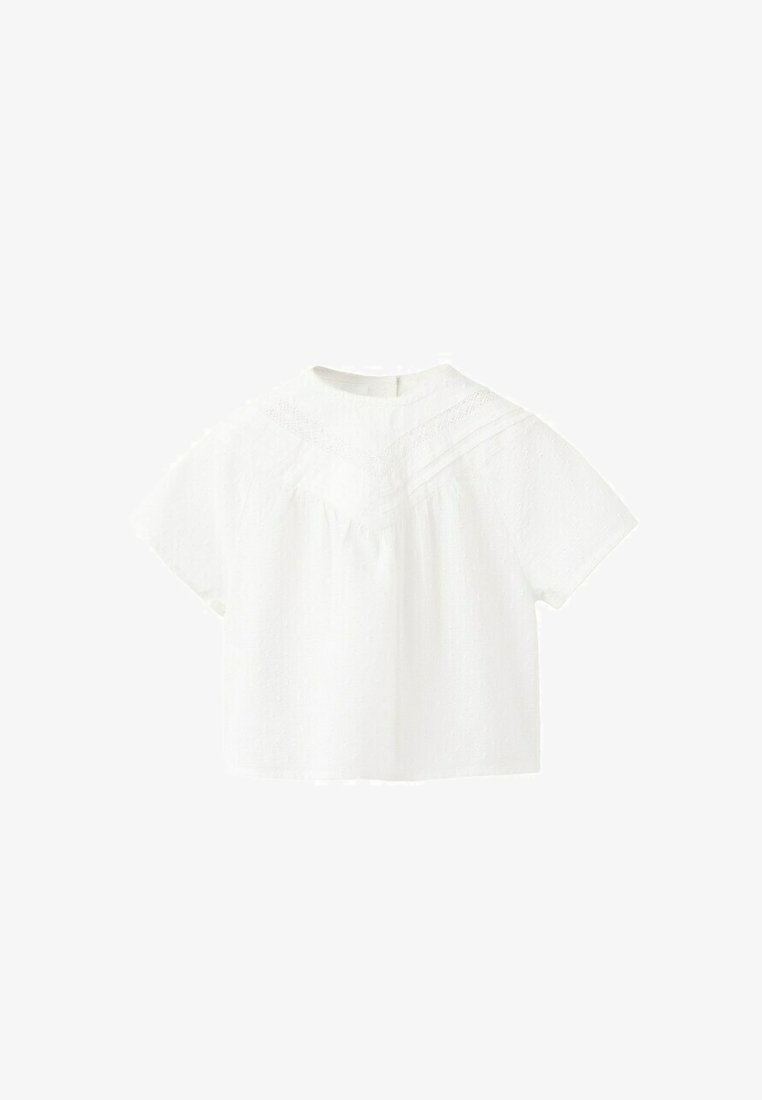 Blouse blanche à manches courtes avec un col montant, un tissu texturé et des détails en dentelle sur la poitrine et les épaules.