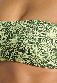 Žalias ir šviesiai geltonas bandeau tipo bikinio viršus su gėlių raštu, reljefine tekstūra ir tamsiai žaliais akcentais.