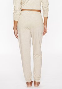 Pantalons de détente beige en tissu doux, avec une taille élastique et des poignets fuselés, vus de derrière.