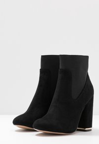 Stivaletti alla caviglia in suede nero con punta arrotondata, pannelli laterali elasticizzati e tacco alto e robusto dotato di un accento dorato alla base.