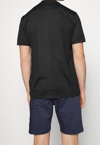 Černé tričko s krátkými rukávy, hladkou strukturou a rovnostranným střihem, kombinované s tmavě modrými šortkami s obráceným lemem.