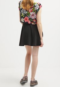 Top de manga corta floral con una falda skater negra, que presenta colores vibrantes, tejido suave y un diseño ligero. Zapatos marrones completan el look.