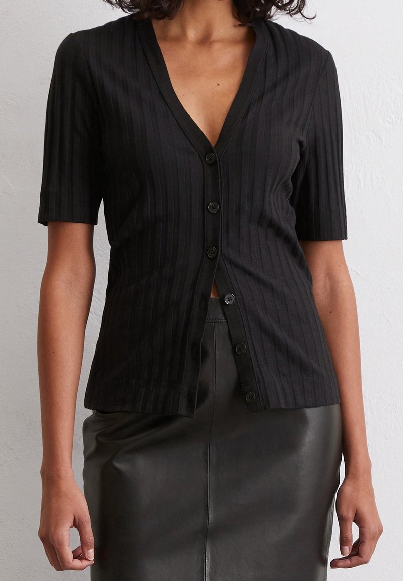 Top negro acanalado de manga corta y botón con un profundo escote en V y cierre frontal de botones, combinado con una falda de cuero negro de cintura alta.