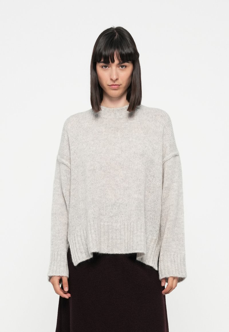 Light grey knitted sweater with a relaxed fit, ribbed hem, and dropped shoulder seams. Soft texture with a boxy shape.
