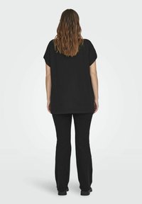 Zwarte oversized top met korte mouwen, gecombineerd met zwarte broek, beide van een zachte, gladde stof. De top heeft een ronde halslijn en een ontspannen pasvorm.