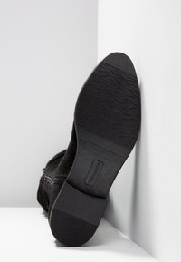 Schwarze Wildleder-Ankle-Boots mit einer strukturierten Gummisohle, die über einen Reißverschluss und eine abgerundete Zehenpartie verfügt. Der Absatz ist niedrig und leicht konturiert.