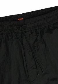 Mustat shortsit, joissa on joustava vyötärö ja kiristysnauha. Kankaan pinnassa on ryppyinen rakenne, jossa on punainen "BOSS"-logomerkkitag.