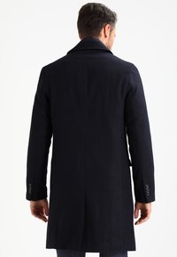 Dark navy wool coat with a long silhouette, notch collar, and buttoned cuffs. Features a clean, minimalist design with no visible patterns.
