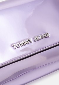 Fialová lakovaná kabelka s lesklým povrchem, vybavená stříbrnými komponenty s vyraženým logem "TOMMY JEANS".
