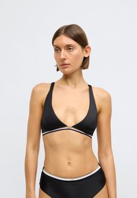 Melns bikini tops ar dziļu V veida kakla izgriezumu. Plānas lences un baltu akcentu josla ar zeltītu detaļu centrā. Gluda auduma tekstūra.