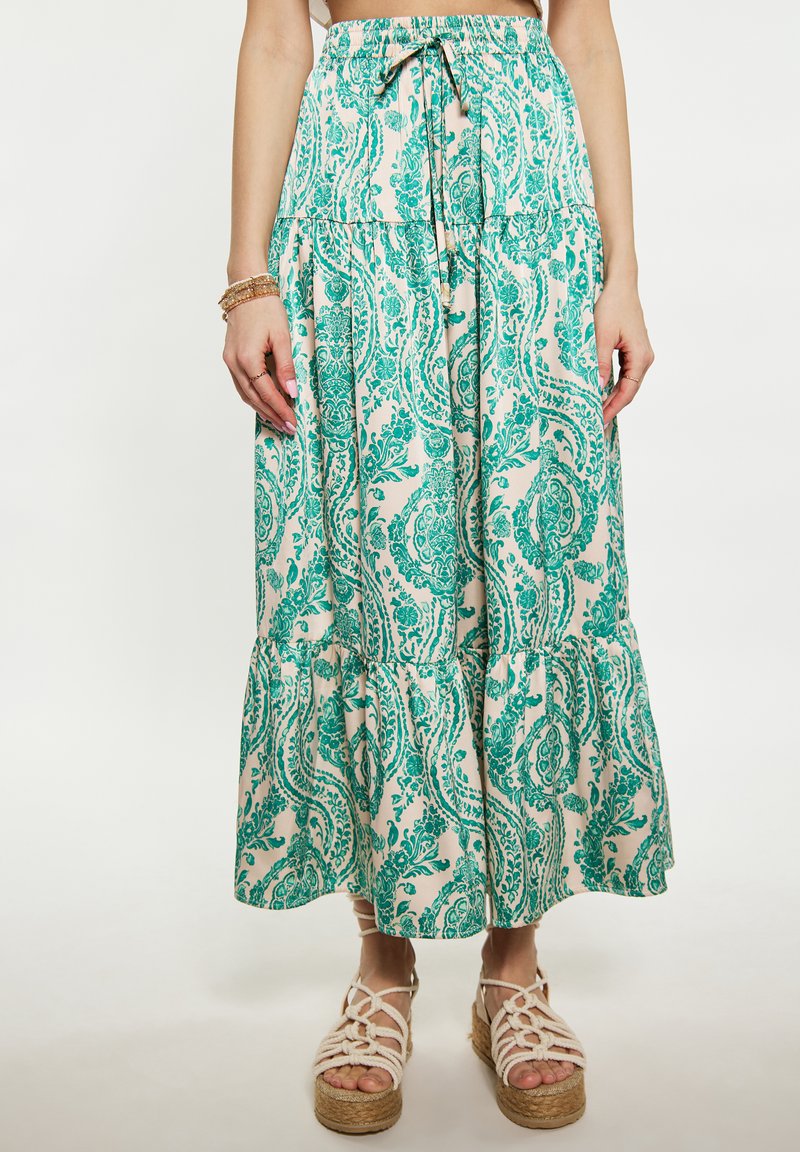 Kremašnja maxi krila s cvjetnim uzorkom u zelenim paisley motivima, s pojasom na vezanje i višeslojnim ruffles rubom. Nosiva s pletenim platformskim sandalama.
