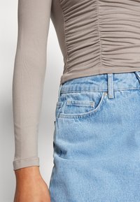 Långärmad, figurnära topp i ljusgrått med draperingsdetaljer, i kombination med höga, ljusblå jeansshorts med en klassisk femficksdesign.