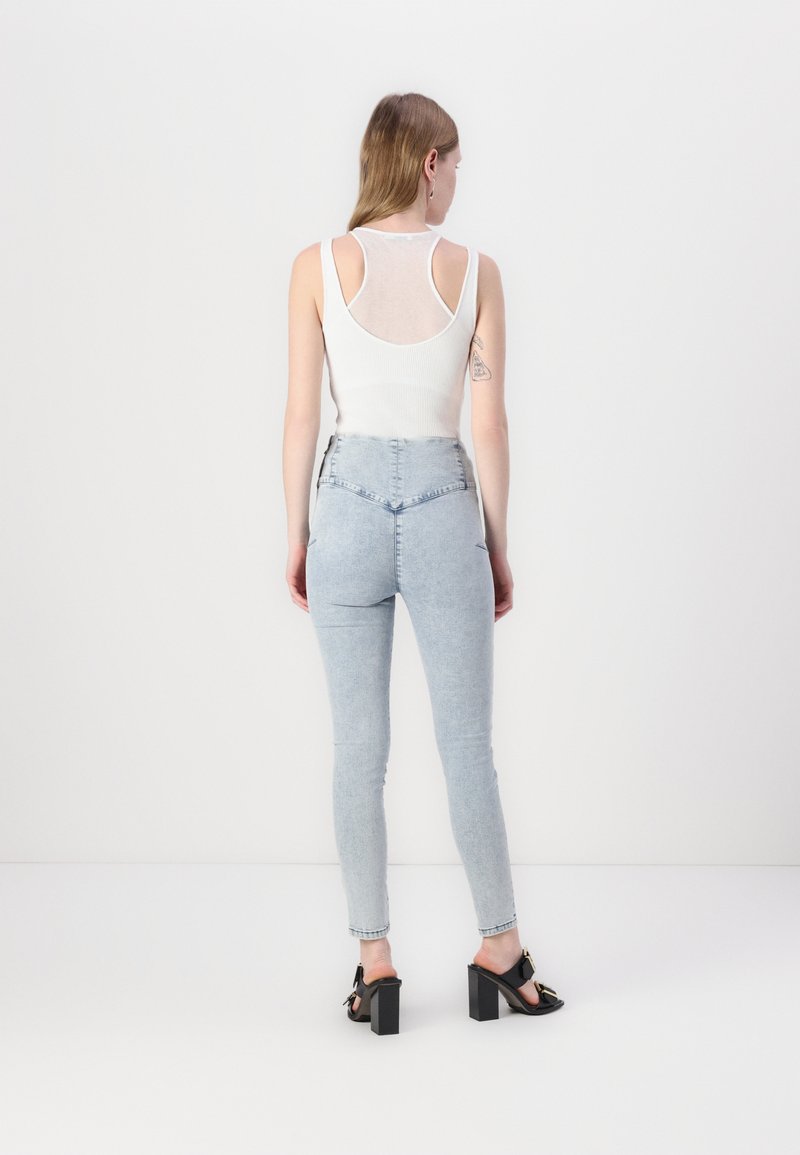 Biała, prążkowana koszulka na ramiączkach z otwartymi plecami, zestawiona z jasnoniebieskimi, wysokimi jeansami skinny oraz czarnymi sandałami na słupku.