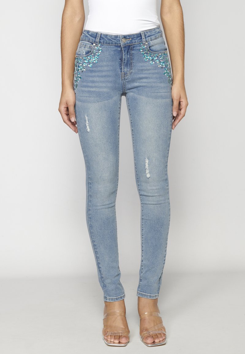 Jeans de mezclilla azul ajustados con adornos florales en turquesa en los bolsillos y ligero desgaste en los muslos.