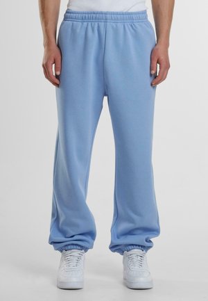 Lyseblå sweatpants lavet af blødt stof. Løs pasform med elastisk talje og manchetter ved anklerne, parret med hvide sneakers.