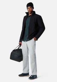 Giacca nera, camicia verde con bottoni, pantaloni bianchi, berretto nero e borsa da viaggio nera. Le sneakers presentano dettagli blu e suole grigie.