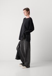 Črna oversize sweatshirt, siva široka denim hlače in kreme barve slip-on čevlji. Prosočna okvirna očala, sproščen videz, minimalističen dizajn.