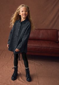 Abito camicia a fantasia nera e grigia con maniche lunghe, abbinato a leggings neri e anfibi neri con lacci.