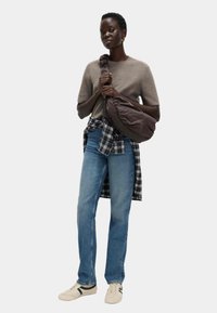 Brązowa torba na ramię, szary sweter z dzianiny, niebieskie dżinsy. Koszula w kratę związana w pasie, białe buty sportowe z czarnymi paskami. Luźny, codzienny styl.